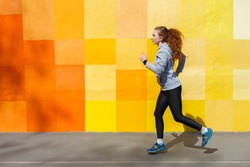 Side view of female athlete running against bright colorful graffiti wall, copy space