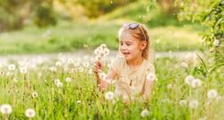 Pretty small girl likes to play with fluffy dandelions on summer meadow
