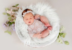 Beautiful newborn baby girl wearing lace costume ana wreath sleeping in basin filled white fur during studio photoshoot. Cute portrait of infant child napping