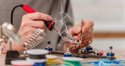 Closeup view of man hands during quadcopter repairing process using soldering iron for wires