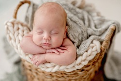 Closeup portrait of newborn baby boy sleeping on knitted blanket in the wicker basket. Infant child put his head in hands