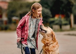 Preteen girl in pink jacket with golden retriever dog smiling at street. Pretty child kid with pet doggy labrador spend time outdoors