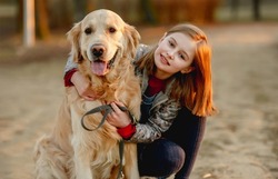 Preteen girl with golden retriever dog sitting in park in beautiful spring autumn day. Adorable female child kid hugging doggy pet outdoors and smiling portrait