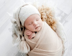 Newborn baby child swaddled in fabric sleeping in basket. Sweet infant kid napping portrait