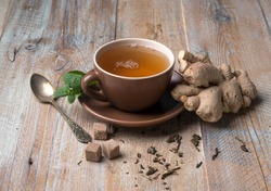 Brown cup of ginger tea with cubes of brown sugar, aged spoon, giner on side