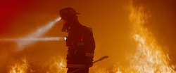 Dramatic silhouette of American firefighter in full gear exploring the huge fire zone
