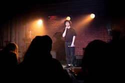 Young Caucasian male comedian performing his stand-up monologue on a stage of a small venue