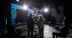 Behind the scenes of virtual production shot - Film crew working with Caucasian female astronaut stuntwoman in a spacesuit hanging on a wires against huge LED screen. Some elements furnished by NASA