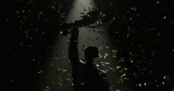 Silhouette of race car driver celebrating the win in a race against bright stadium lights, rising a trophy over his head