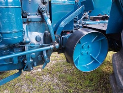 Partial view of an old and restored tractor in blue with a view of the belt drive line for a transmission belt and the steering and coupling linkage. 