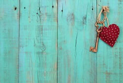 Bronze skeleton house key and red country fabric heart with stars hanging on antique teal blue old wood door; Valentines Day, real estate and home concept background with wooden painted copy space