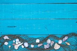 Seashells with fish net border on antique rustic teal blue wood background; blank beach sign with painted wooden copy space