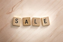 The Words Sale are spelled out in wooden letter tiles on a light wood background.
