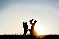 A silhouette of a happy family of four people, mother, father, baby, and child, and their dog in front of a sunsetting sky, with room four copy space or text