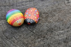 Two hand painted rainbow love bugs on rocks are sitting on a natural wood background.