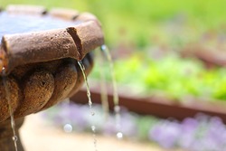 Close up on water dripping out of stone fountain in beautiful spring flower garden.  Shallow Depth of Field.