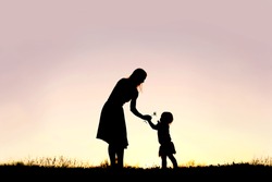 A silhouette of a sweet toddler girl is handing her mother a Daisy flower, in a meadow outside at sunset on a summer day.