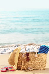 Summer beach bag with straw hat,towel,sunglasses and flip flops on sandy beach