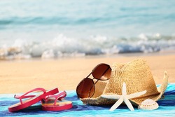 Summer straw hat with towel,sunglasses and flip flops on sandy beach