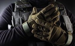 Photo of a fully equipped soldier in black armor tactical vest and gloves standing on black background closeup front view.