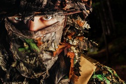 Photo of a male hunter face in panama hat and ghillie forest camouflaged suit.