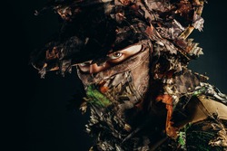 Photo of a male hunter face in panama hat and ghillie forest camouflaged suit.