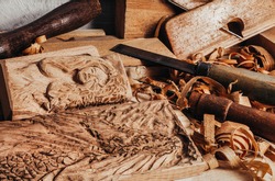 Photo of wooden old fashioned planes with carving chisels laying on workbench table with dragon and woman goddess bas-relief wooden sculpture.