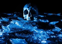 Horror scary photo of human skull laying on cracked ice surface ground.