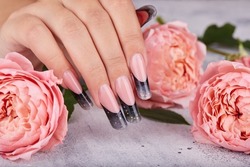 Hand with long artificial manicured nails colored with black nail polish and pink rose flowers