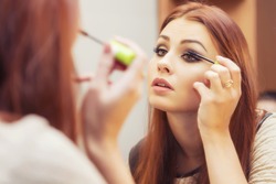 Brunette woman applying make up (paint her eyelashes) for a evening date in front of a mirror. Focus on her reflection
