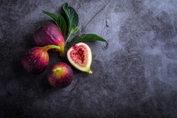 Fresh ripe figs with green leaf and on dark table black background. Healthy Mediterranean fig fruit. Beautiful blue-violet figs with empty copy space close up.