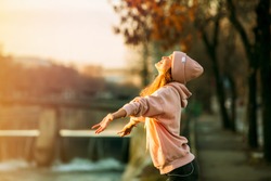 cool hipster young girl in pink hoodie standing by a river in the city very happy smiling to the sun and enjoying it, on autum or springtime