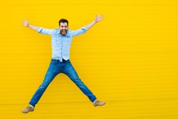 handsome man casual dressed celebrating and jumping on yellow background