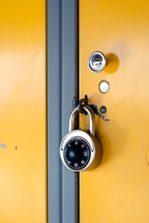 Yellow School Locker with Black Combination Lock - The door of a yellow metal locker in the hallway of a school, locked with a stainless steel combination lock with a black knob on the face.