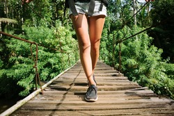 Woman's legs with backpack walking across hanging bridge in tropical forest