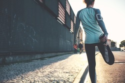 Athlete woman preparing for running on the city street. Legs warming and stretching. Sport tight clothes. Blurry background. Horizontal