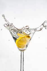 A slice of lemon splashing into a martini glass on white background - high speed photography. Selective focus.
