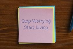 Top view of Stop Worrying Start Living note on the wooden desk with pen aside.