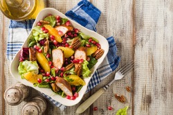 Spring salad with chicken, pomegranate, orange, pecan nuts and honey. Old table background. Top view. Wooden table background. 