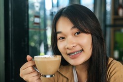 Close up, Portrait young beautiful woman with coffee latte art  in coffee shop, she holding and inhale aroma of coffee and admire the beauty of milk froth in coffee cup