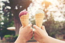 Woman's hands holding melting ice cream waffle cone in hands on summer light nature background