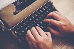 Hands typing on vintage typewriter on wooden table.