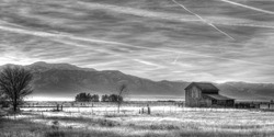 Horizontal Black and White Image of an Old Barn, Trees, Meadow and Mountains at Sunrise.  