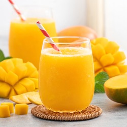 Fresh mango juice. Close up design concept of smoothie cold drink in a glass cup with paper straw on gray table background.