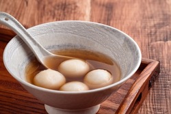 Close up of sesame big tangyuan (tang yuan, glutinous rice dumpling balls) with sweet syrup soup in a bowl on wooden table background for Winter solstice festival food.