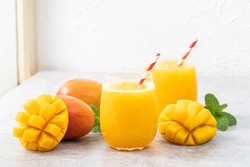 Fresh beautiful delicious mango juice. Close up design concept of smoothie cold drink in a glass cup with paper straw on gray table background.