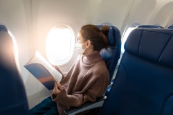 A young woman wearing face mask is traveling on airplane , New normal travel after covid-19 pandemic concept 