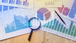 Magnifying glass and documents with analytics data lying on table,selective focus