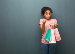 Young black woman doing a gesture of need. She is holding a shopping bags.