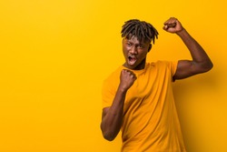 Young black man wearing rastas over yellow background raising fist after a victory, winner concept.